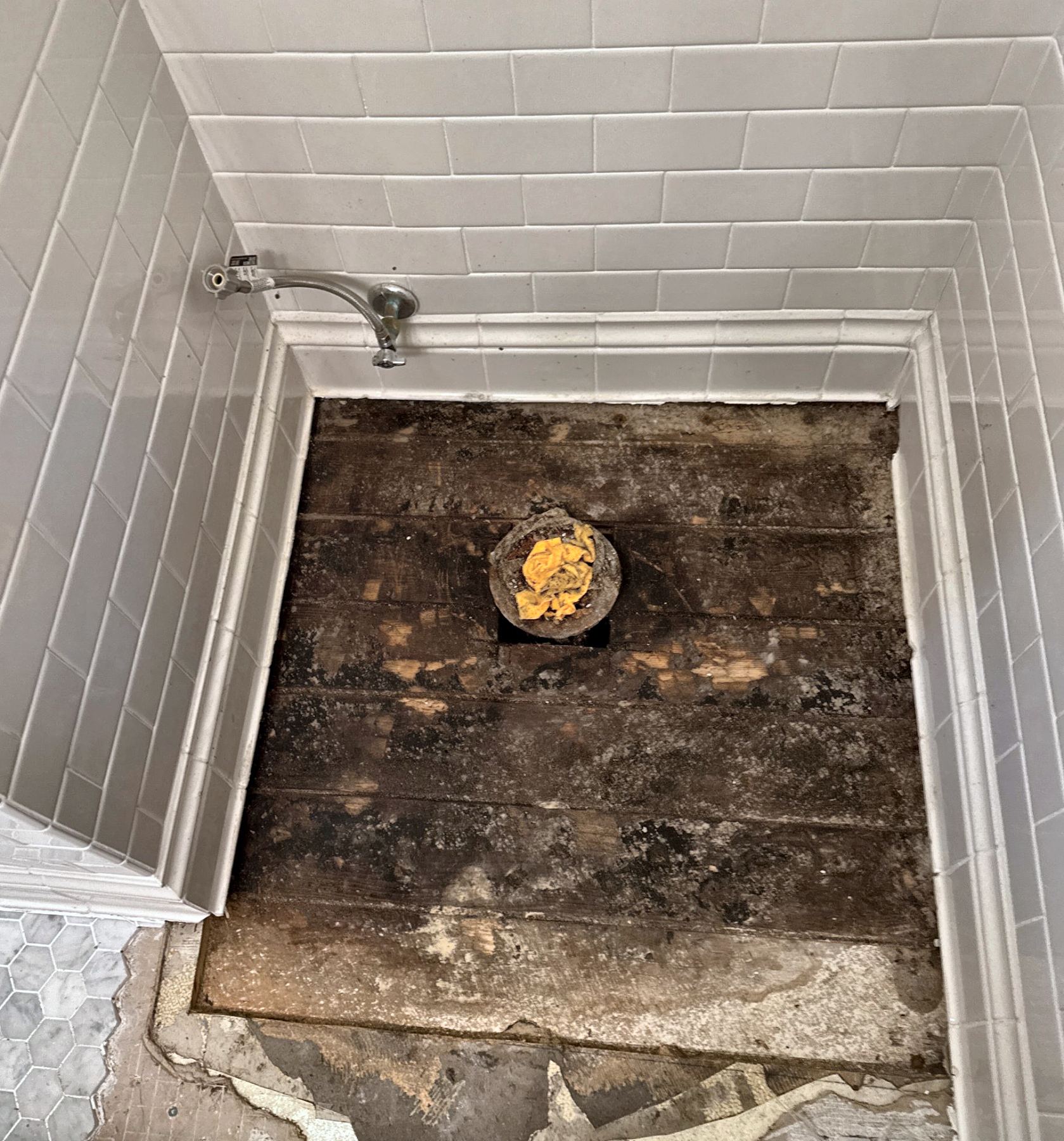Hex tile removed down to the water-stained plank subfloor, left open to dry during a Portland bathroom floor repair