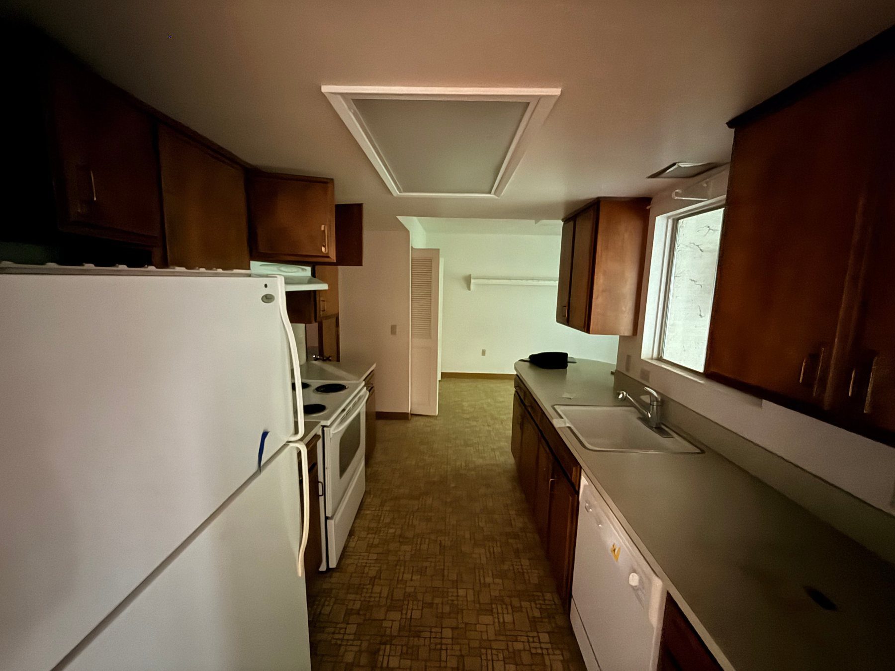 Dark, dated kitchen before renovation with brown cabinets and worn flooring